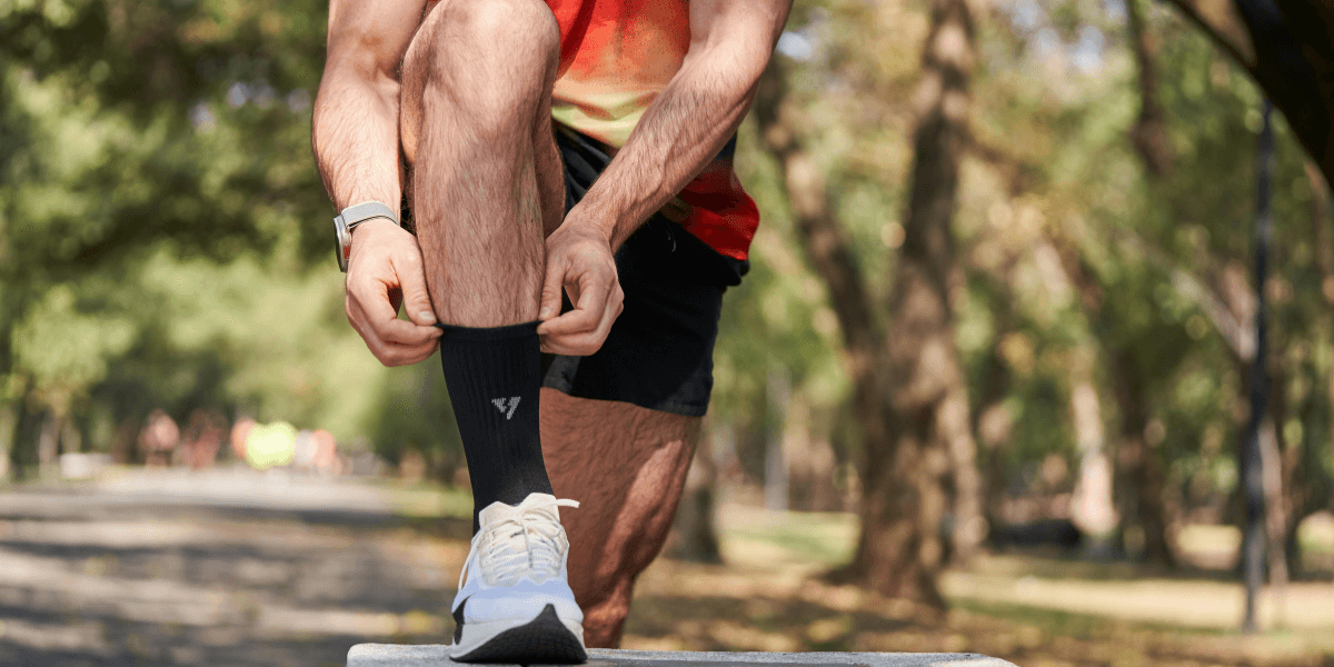 A person adjusting their sock while outdoors in athletic wear and sneakers