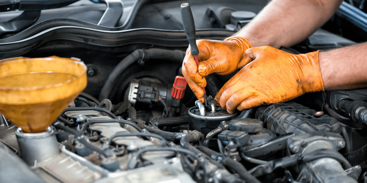 Mechanic wearing orange gloves working on an engine with tools and oil funnel