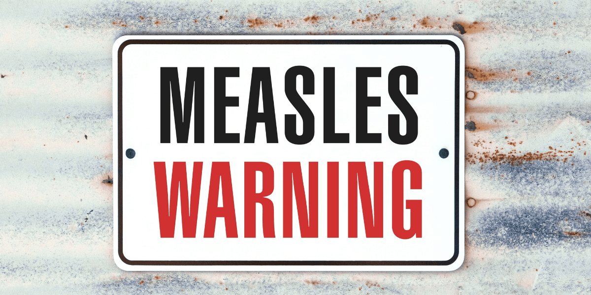 Sign displaying "MEASLES WARNING" in bold black and red letters on a weathered background