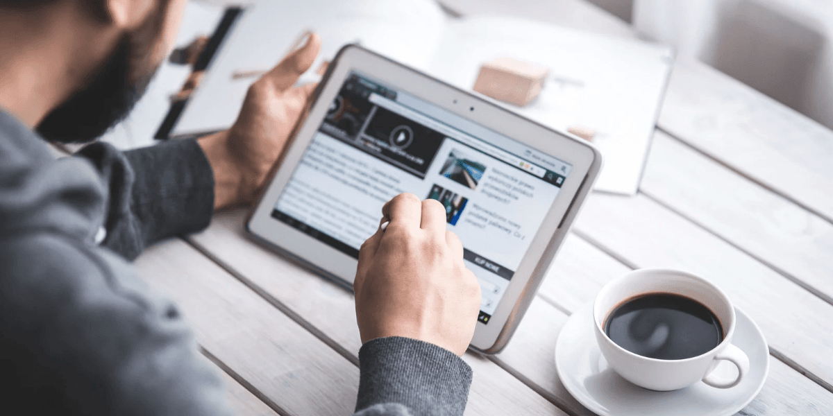 Person using a tablet to read news while sitting at a table with coffee