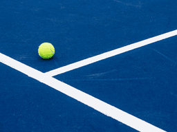 A bright yellow tennis ball on a blue court with white lines