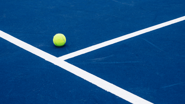 A bright yellow tennis ball on a blue court with white lines
