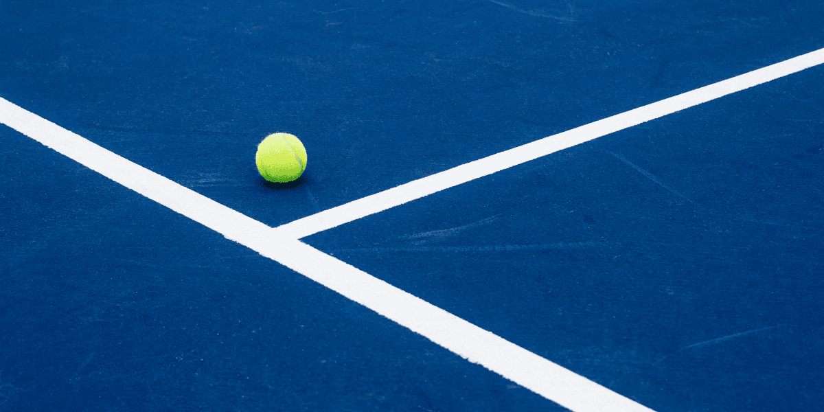 A bright yellow tennis ball on a blue court with white lines
