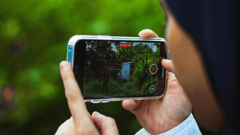 Person holding a smartphone, recording a video of a green outdoor scene