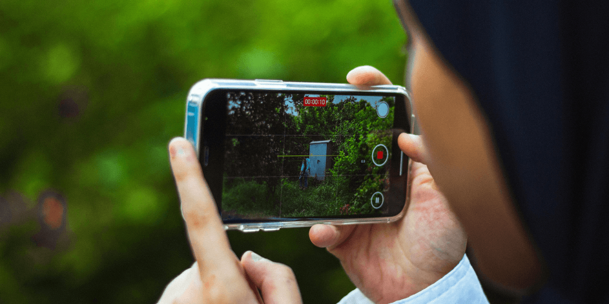 Person holding a smartphone, recording a video of a green outdoor scene