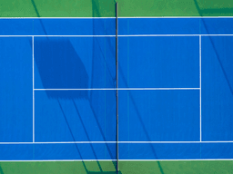 Aerial view of a blue tennis court with white lines and green surroundings