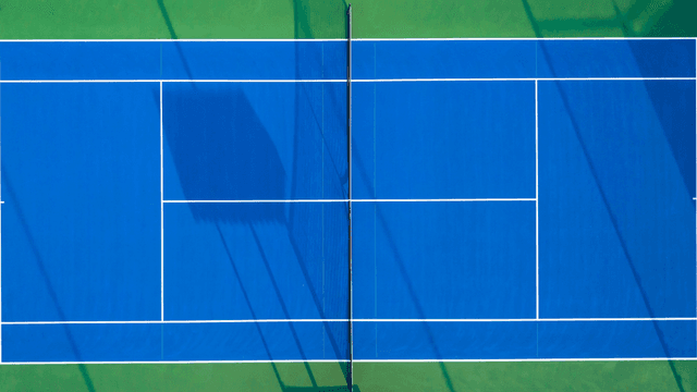 Aerial view of a blue tennis court with white lines and green surroundings