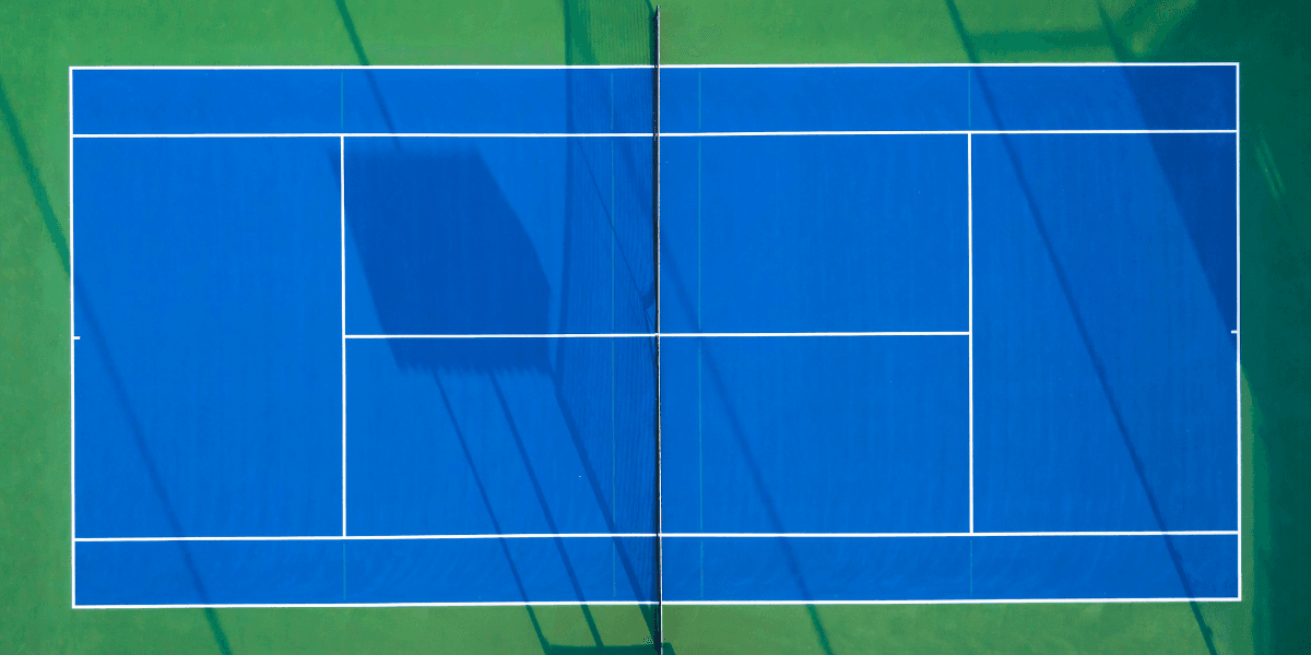 Aerial view of a blue tennis court with white lines and green surroundings