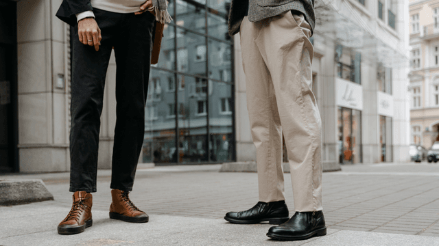 Two individuals stand on a city street, showcasing stylish boots and casual trousers.