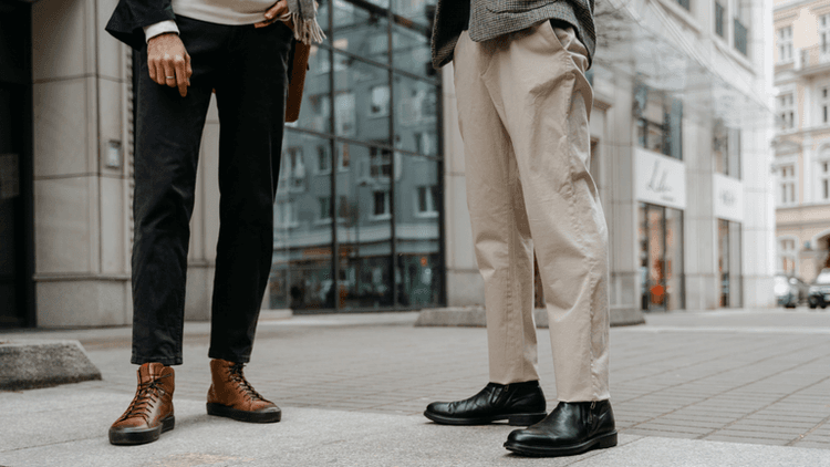 Two individuals stand on a city street, showcasing stylish boots and casual trousers.