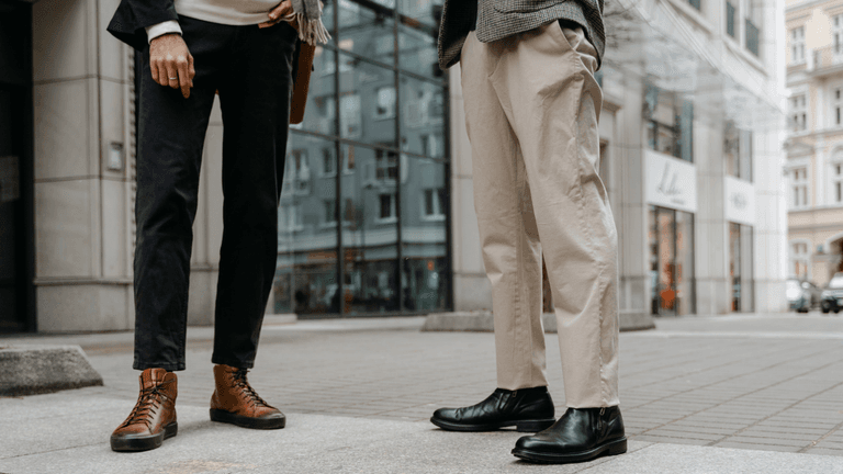 Two individuals stand on a city street, showcasing stylish boots and casual trousers.