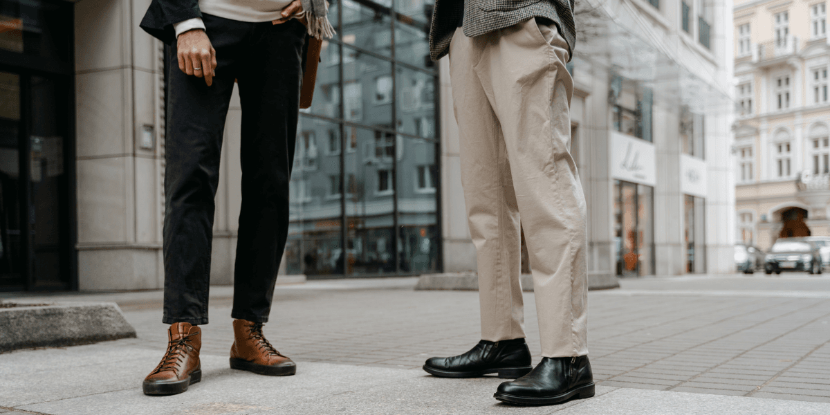 Two individuals stand on a city street, showcasing stylish boots and casual trousers.