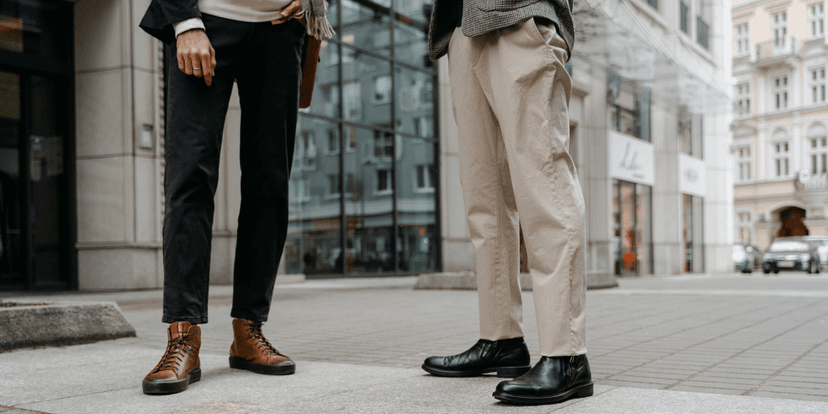 Two individuals stand on a city street, showcasing stylish boots and casual trousers.