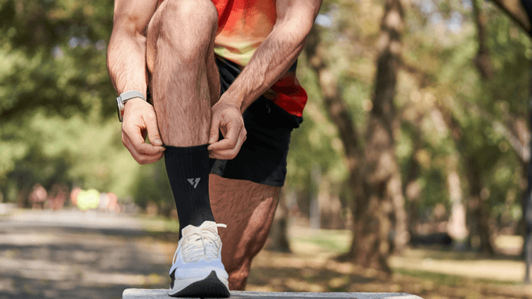 A person adjusting their sock while outdoors in athletic wear and sneakers