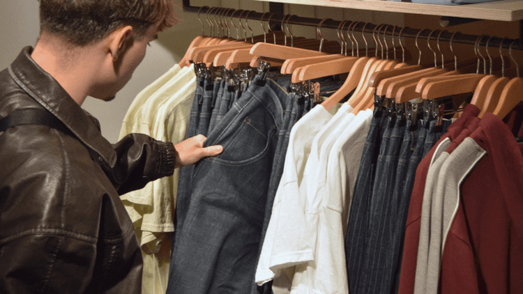 Person selecting jeans from a clothing rack in a store display
