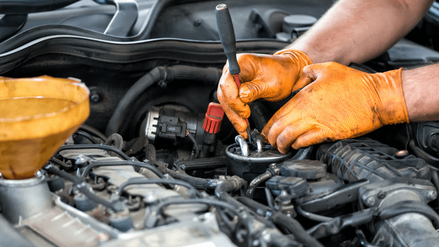 Mechanic wearing orange gloves working on an engine with tools and oil funnel