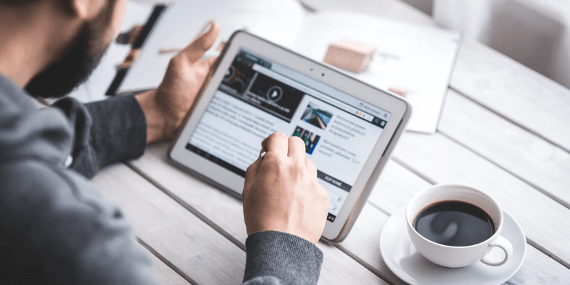 Person using a tablet to read news while sitting at a table with coffee